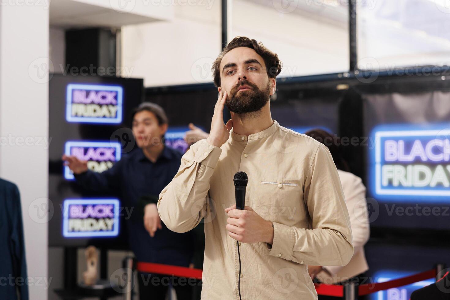 TV reporter live broadcasting talking about Black Friday lines in local shopping mall, holding microphone and looking at camera. Young man correspondent covering news about sales season in retail photo