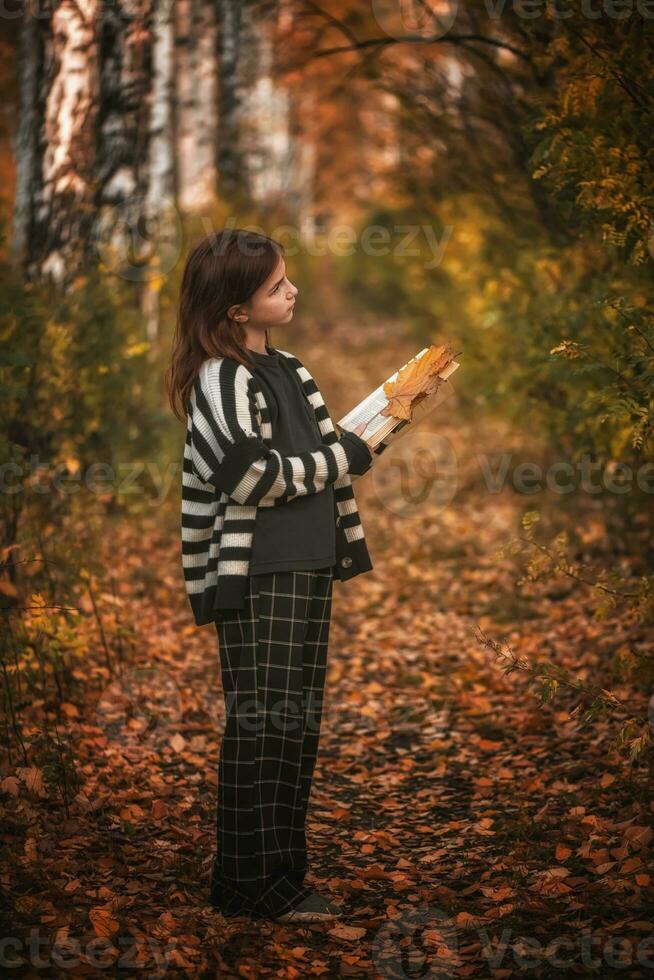 niña con pecas con un libro entre otoño hojas foto