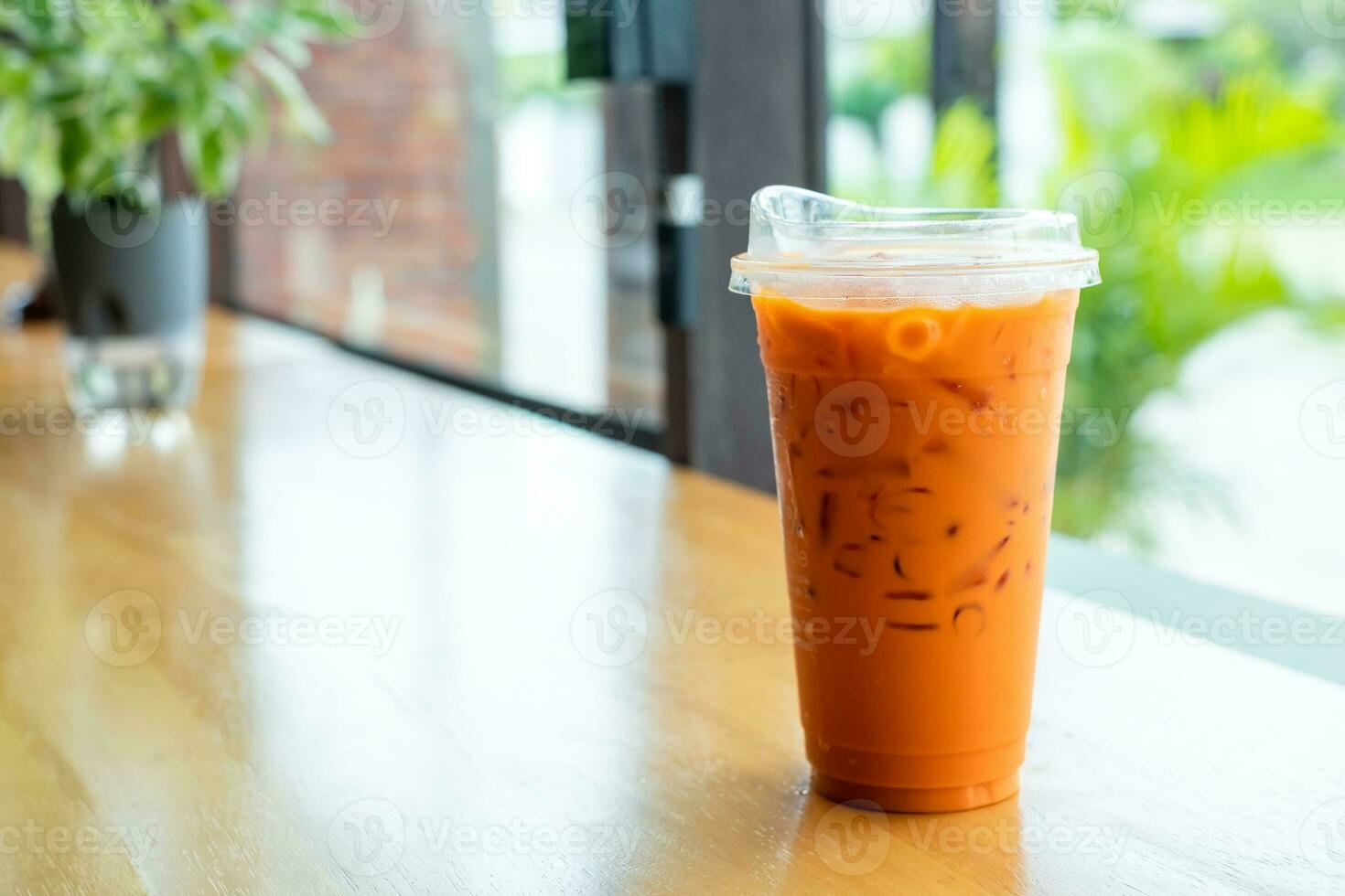 Iced Thai milk Tea in a plastic cup on a wooden table in a coffee shop., Cheddar is a traditional Thai drink that has long been popular. photo
