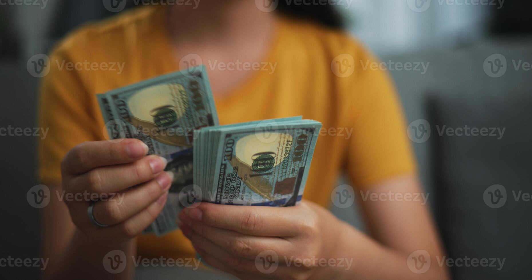 Portrait close up hands of young Asian woman enjoy counting cash dollars banknotes on sofa in the living room at home. photo
