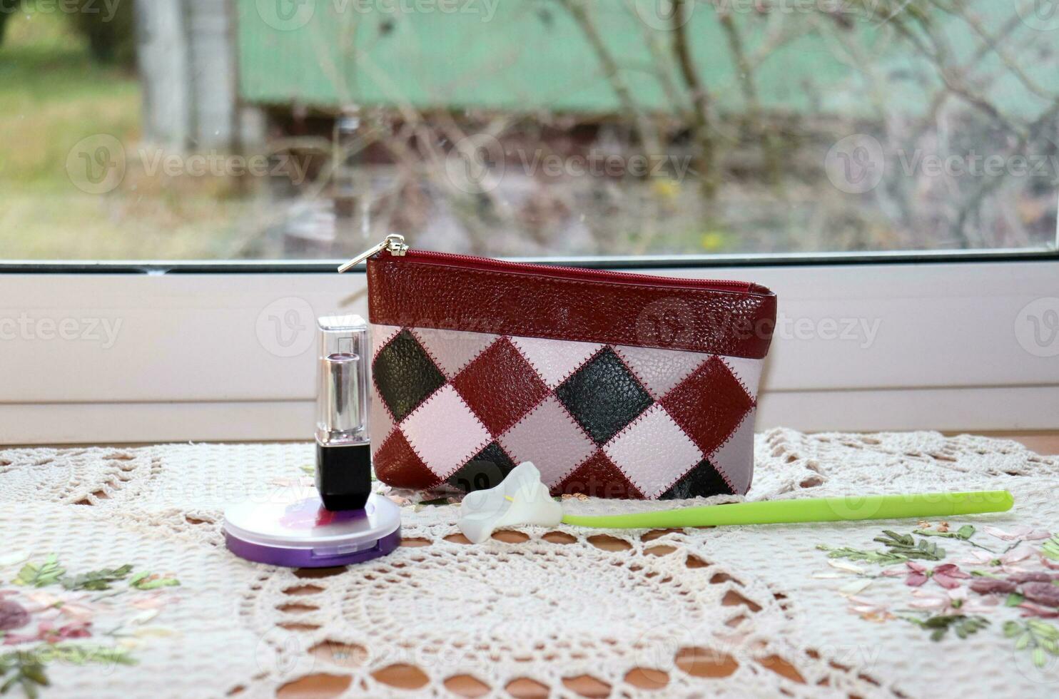 Cosmetic bag, powder, lipstick with an artificial calla flower on a table with a napkin near the window, horizontal photo