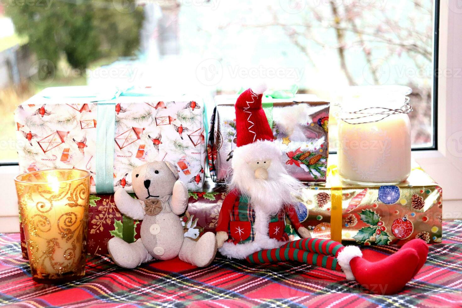 Christmas gifts and candles with toy gnome and teddy bear near the window, horizontal photo, close-up photo