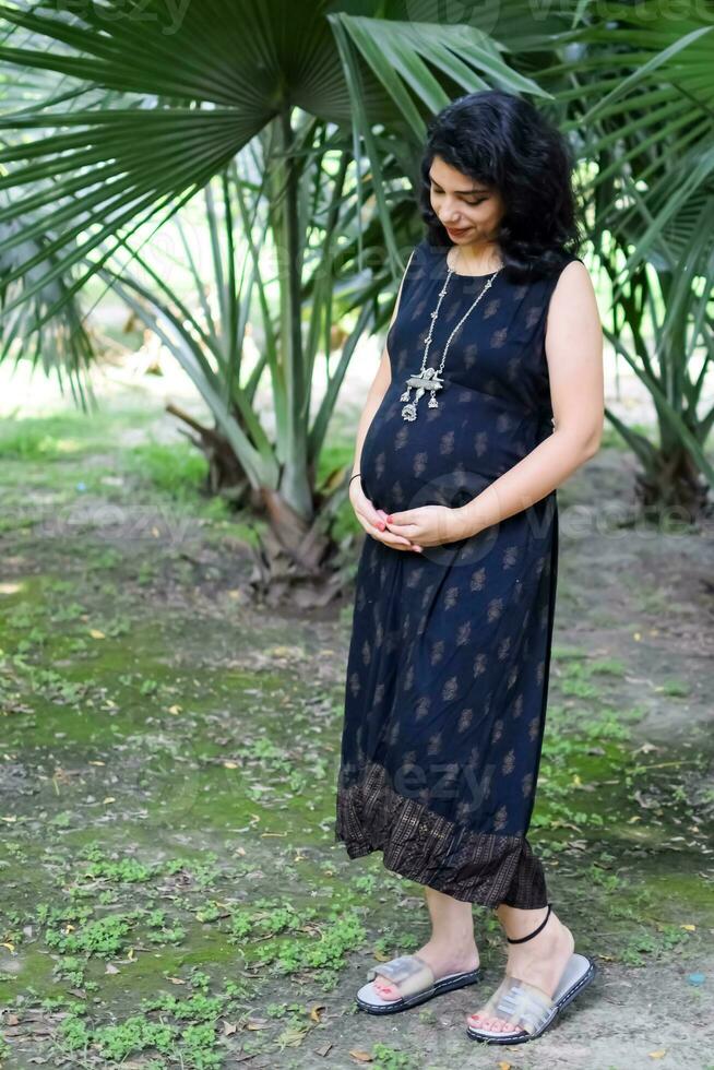 https://static.vecteezy.com/system/resources/previews/033/887/693/non_2x/a-pregnant-indian-lady-poses-for-outdoor-pregnancy-shoot-and-hands-on-belly-indian-pregnant-woman-puts-her-hand-on-her-stomach-with-a-maternity-dress-at-society-park-pregnant-outside-maternity-shoot-photo.jpg