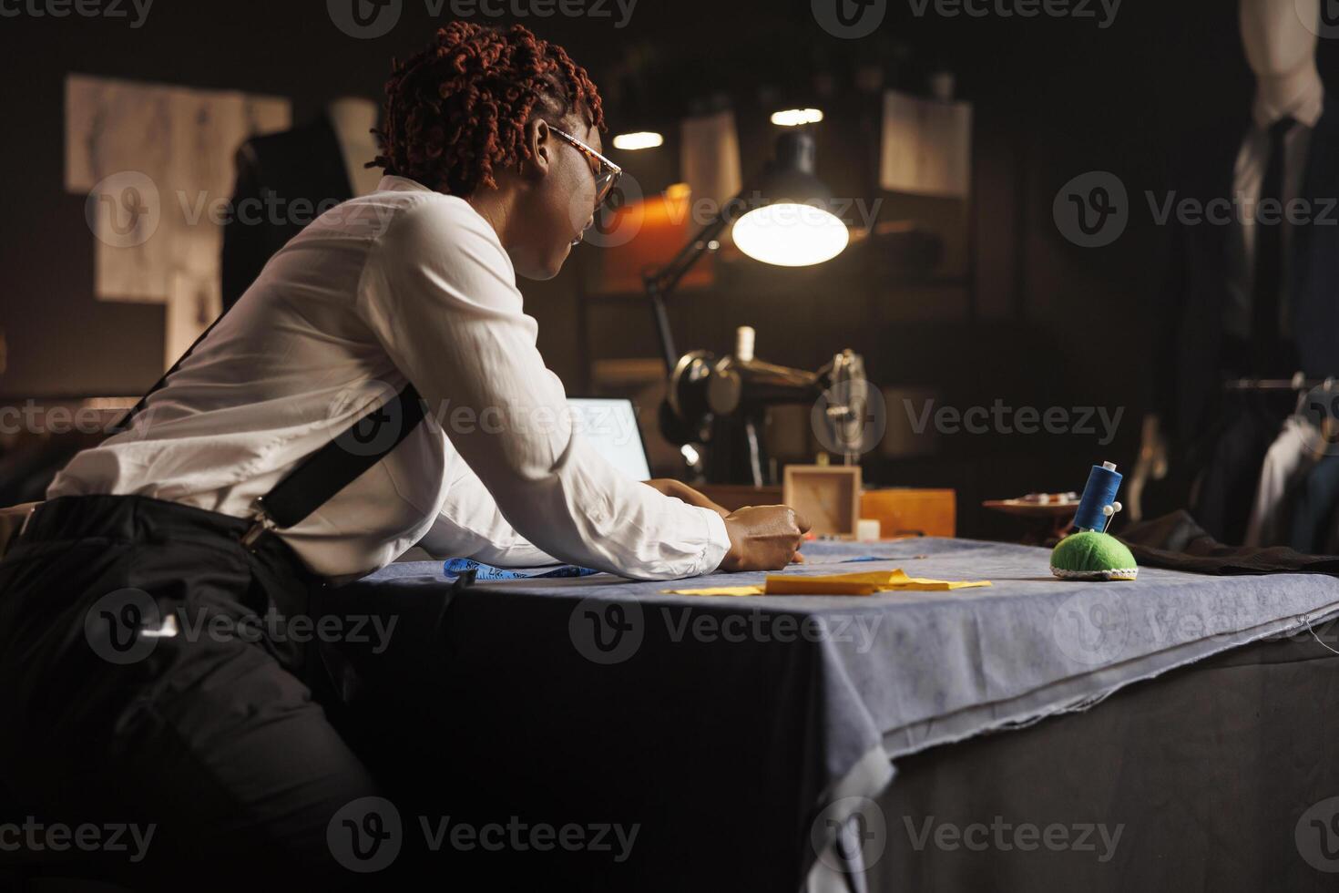 African american suitmaker doing fabric measurements in professional tailoring studio. Expert dressmaker working on manufacturing custom made stylish sartorial outfit for client photo