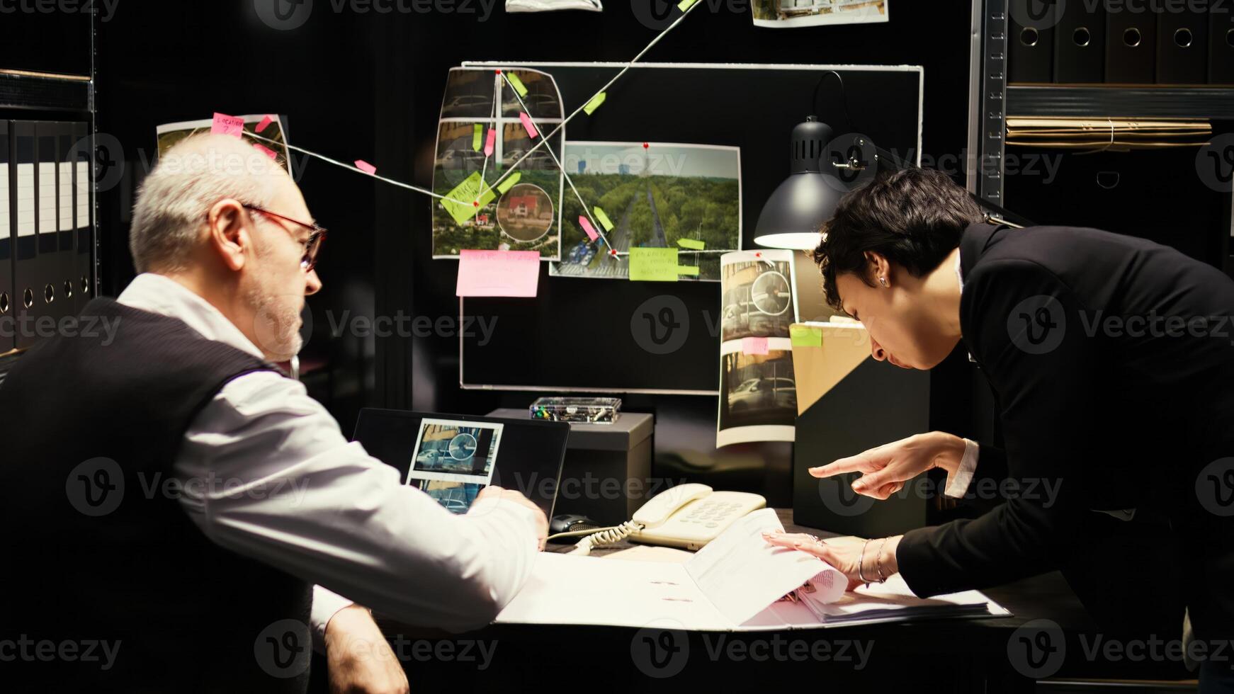 Experts team undertaking investigation with incriminating proof in incident room, examining police case files. Inspector working with detective to carry out investigatory law services. photo