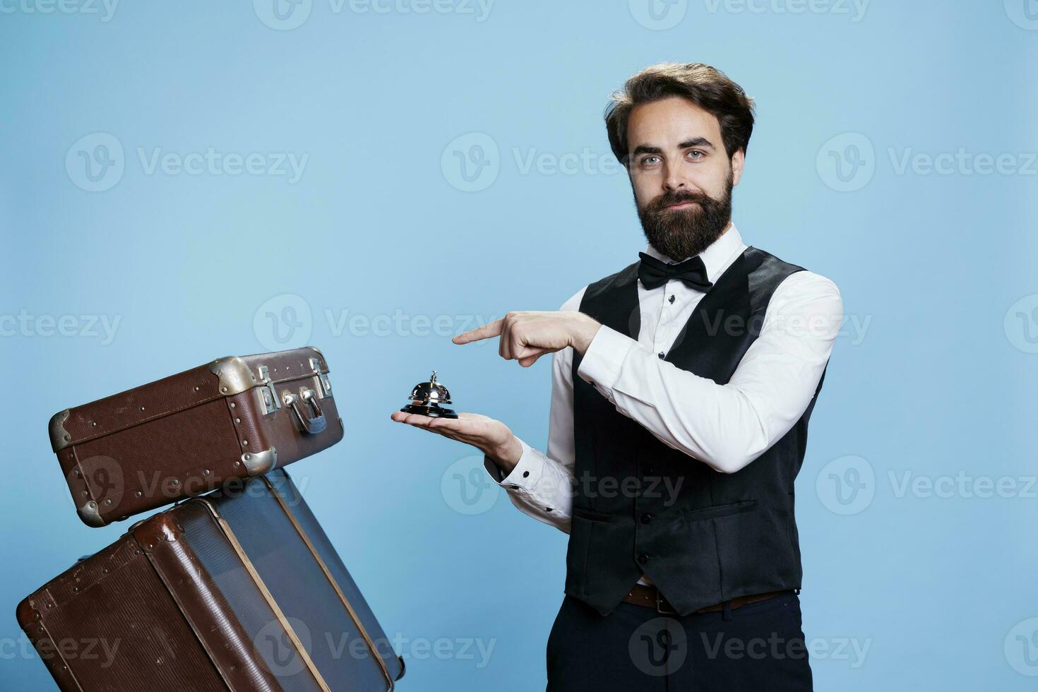 masculino botones con maletas y campana, utilizando a anillo para Servicio o asistencia a hotel en hospitalidad industria. joven hombre trabajando como portero o botones manejo carretilla pantalones equipaje. foto