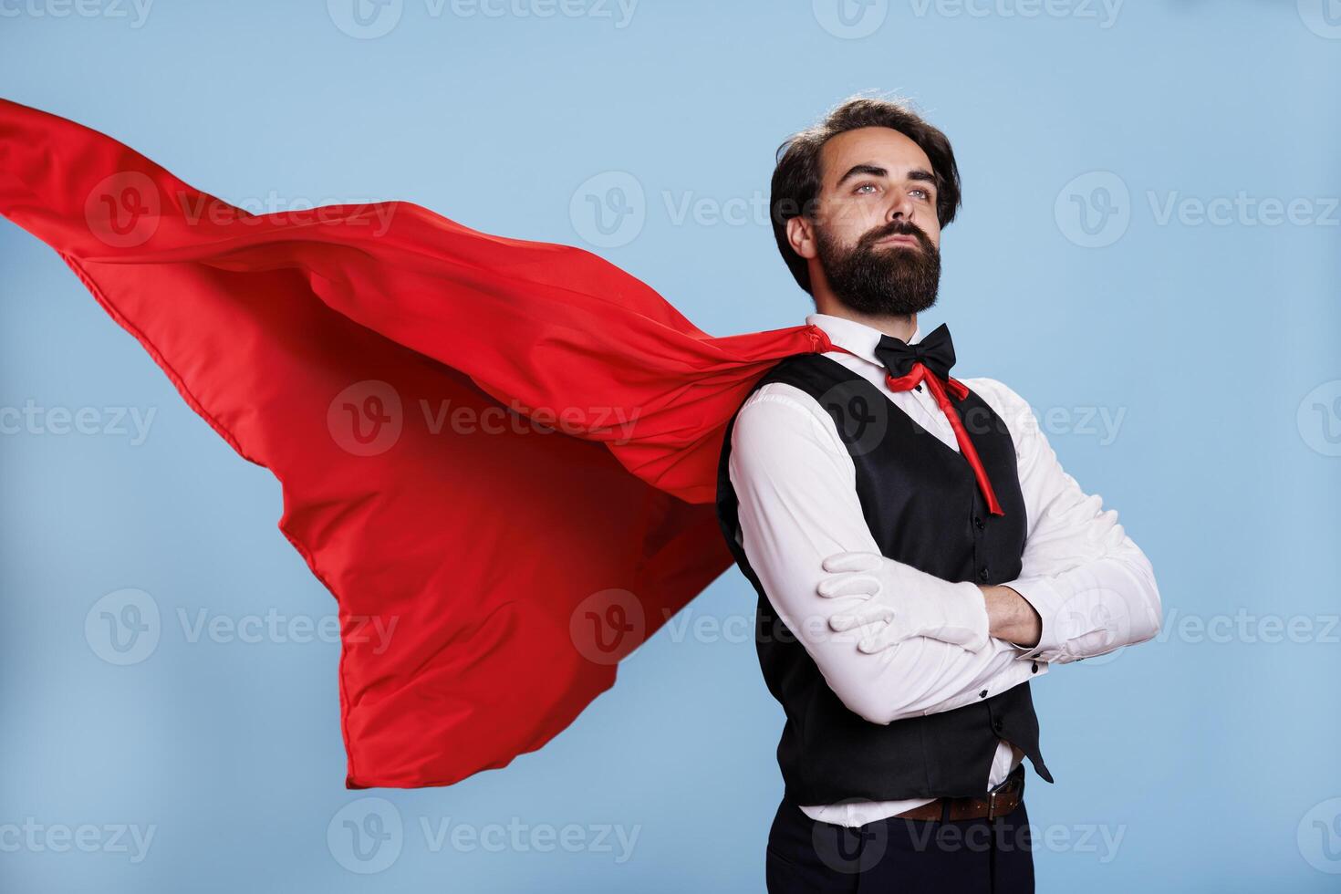 Model superhero with cartoon cape posing over blue background, wearing fantasy leader costume with suit and tie in studio. Young adult acting powerful to protect people, strong superhuman. photo