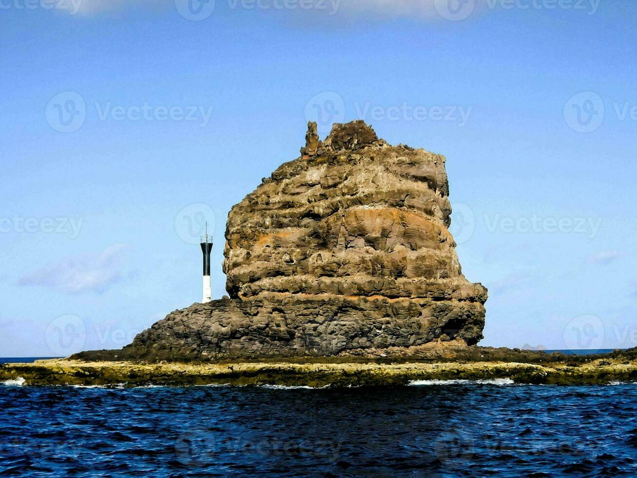 a lighthouse on a rock in the middle of the ocean photo