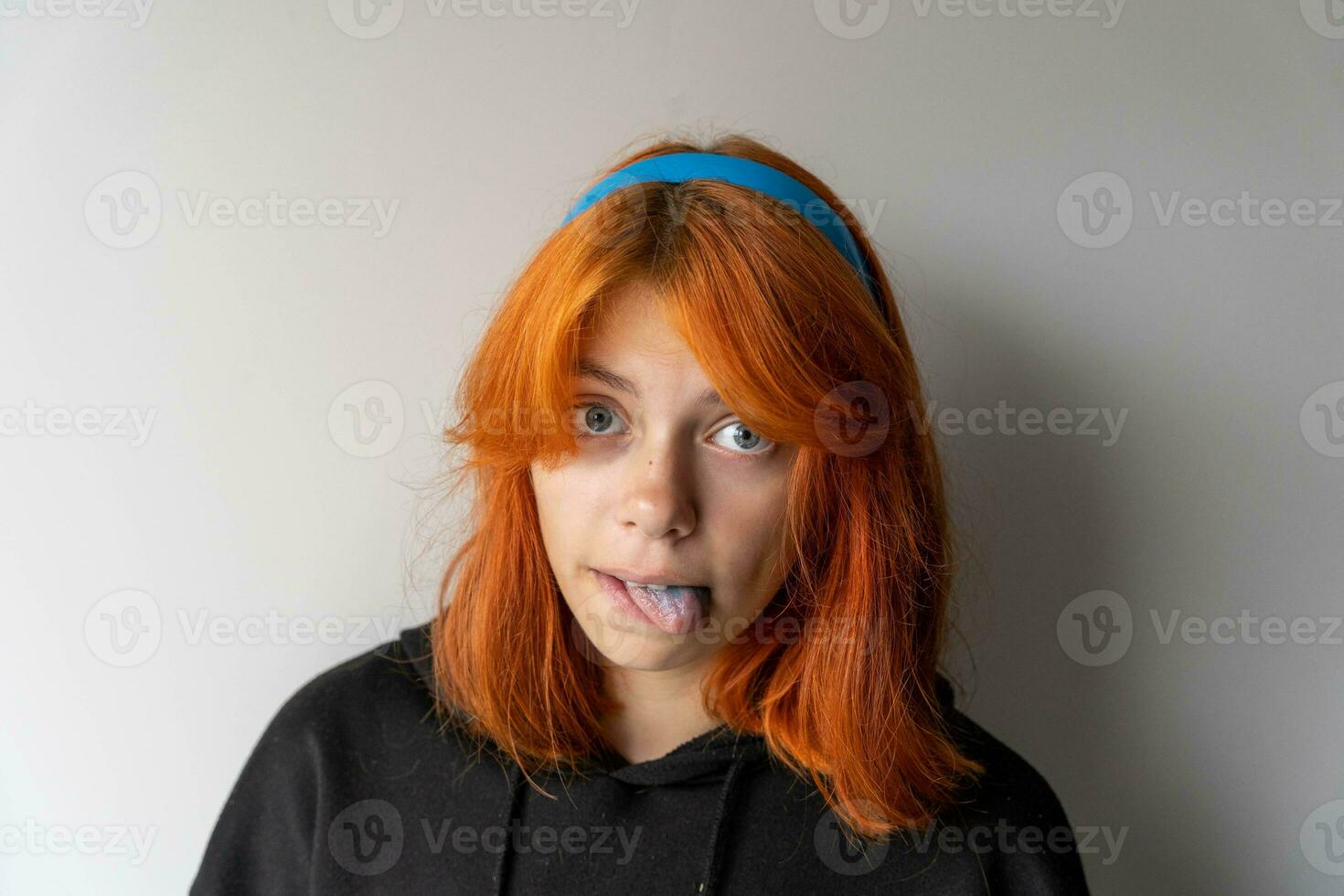 funny teen girl with red hair shows blue tongue. The girl is fooling around photo