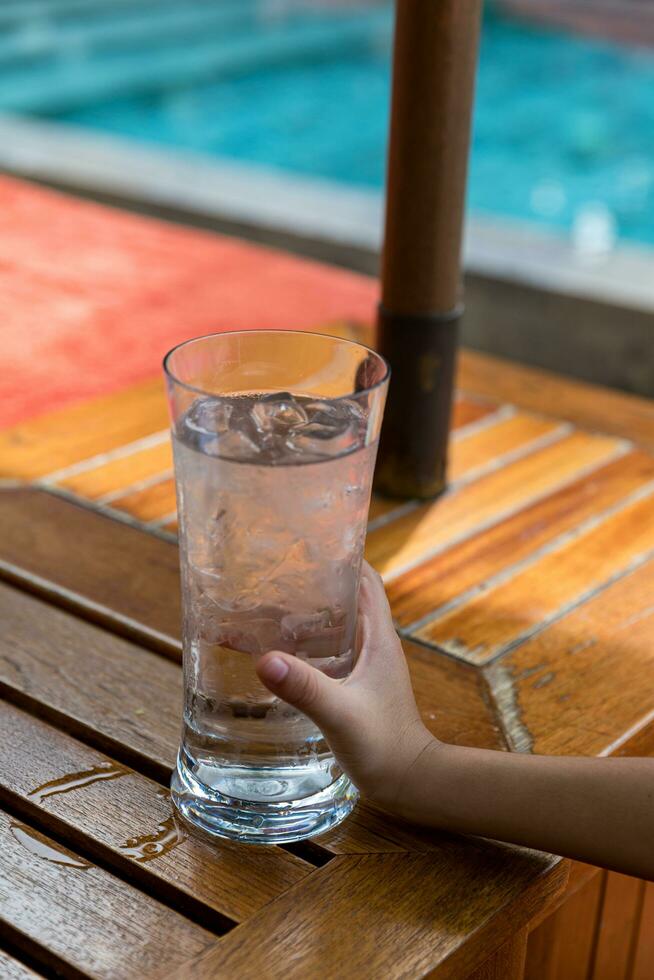 Child's hand holding a glass of cold water by the swimming pool photo