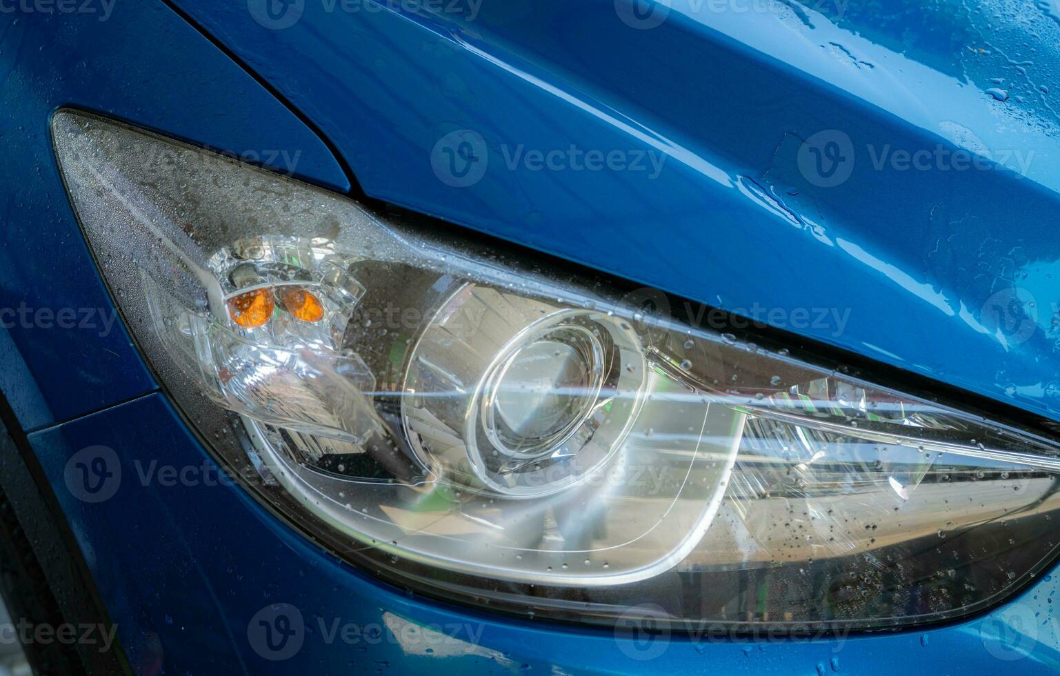 Closeup headlamp of blue car are washing with water. Car care service business concept. Car wash service. Car covered with drops of water after cleaning with high pressure water spray. Auto care. photo