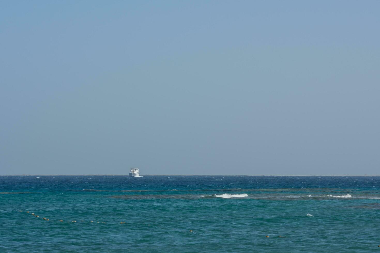 white boat at the horizon of the blue sea with blue sky photo