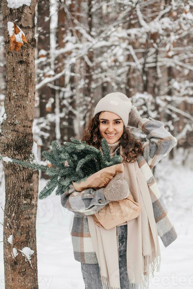 A cute girl with her hand on her hat in a snowy forest holds a package with fir nobilis photo