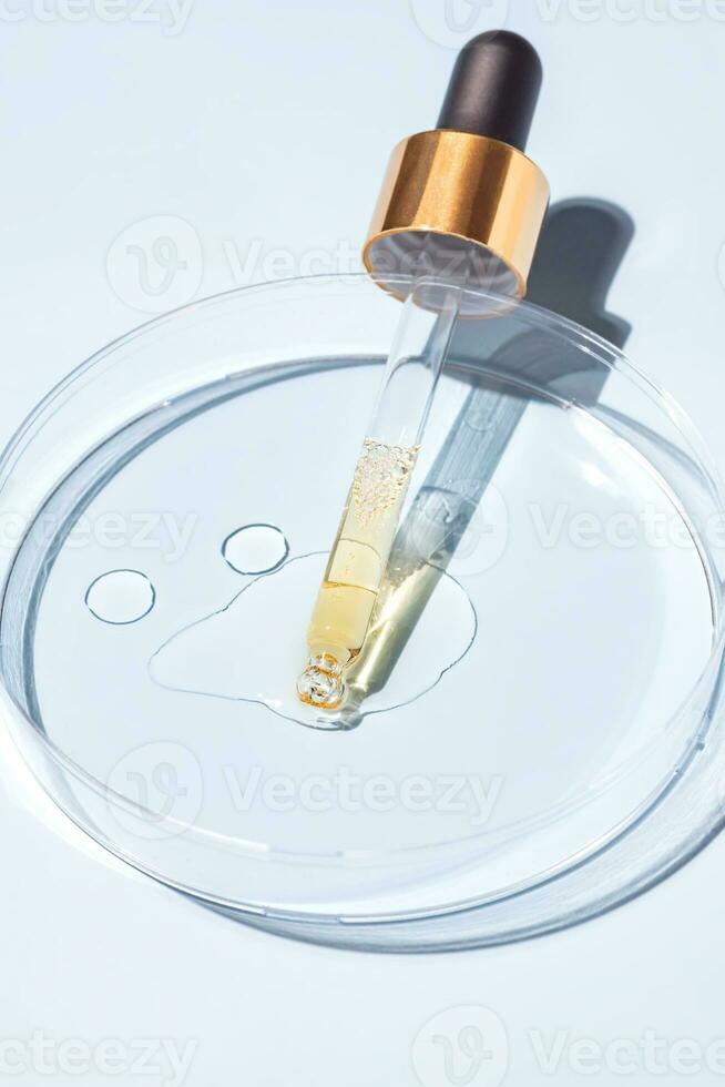close up of pipette with pouring liquid serum and shadows in petri dish on beige background. Trendy cosmetics shot with hard shadows. photo