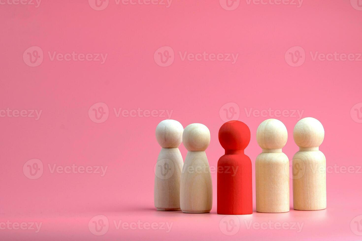 Red wooden doll Among the normal wooden dolls on a pink background. Concept of individuality, assertiveness, Leadership, and teamwork photo