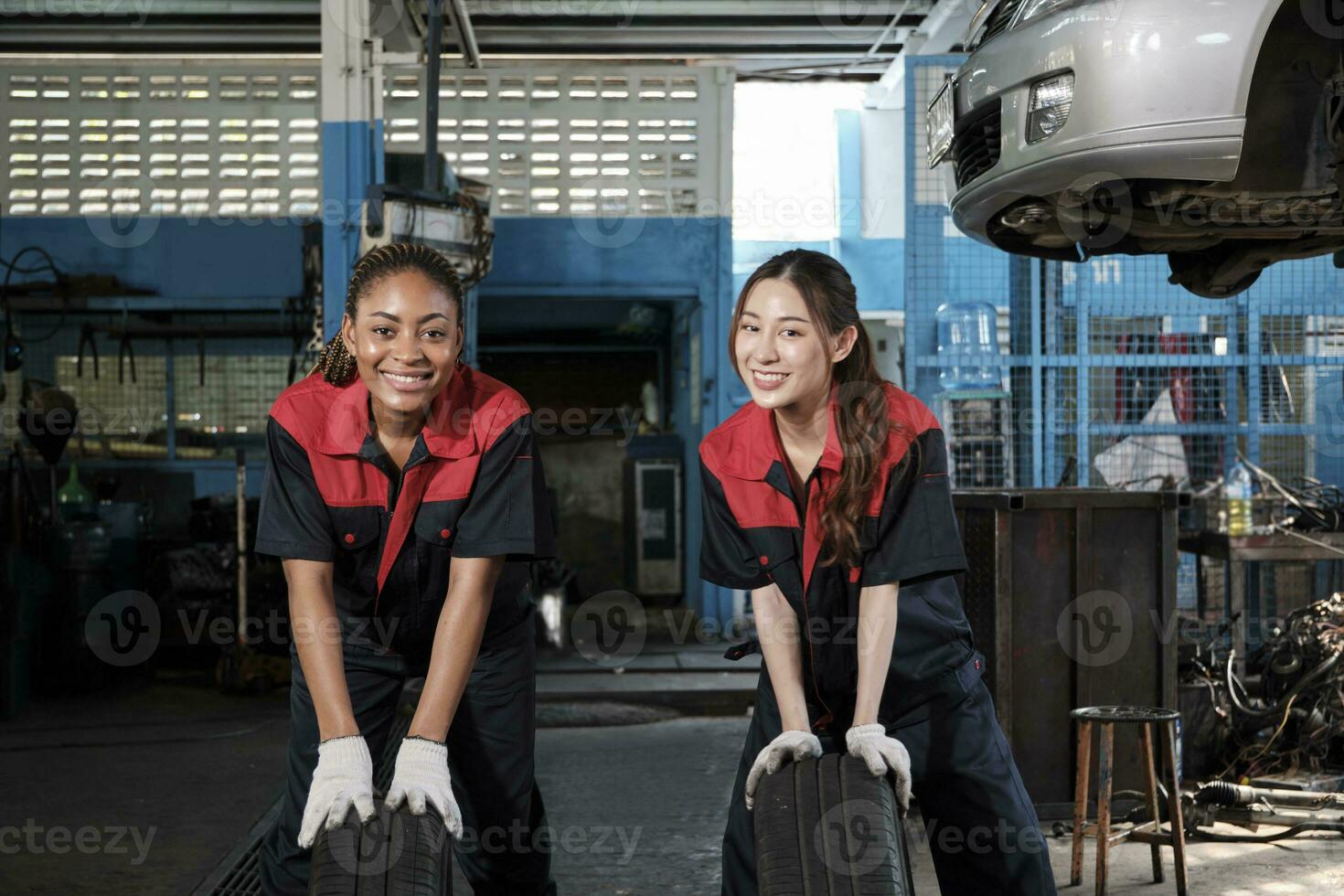 Two diverse female automotive mechanic worker partners compete to push car wheels for change and repair at garage, vehicle maintenance service jobs, industry occupation, and professional labor works. photo
