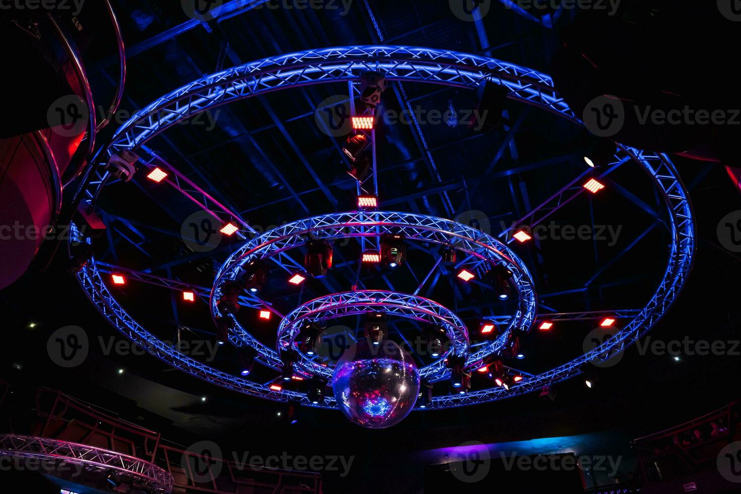 night disco club with neon blue violet red light, disco mirror ball and bright floodlight with round metal frame luminous construction photo