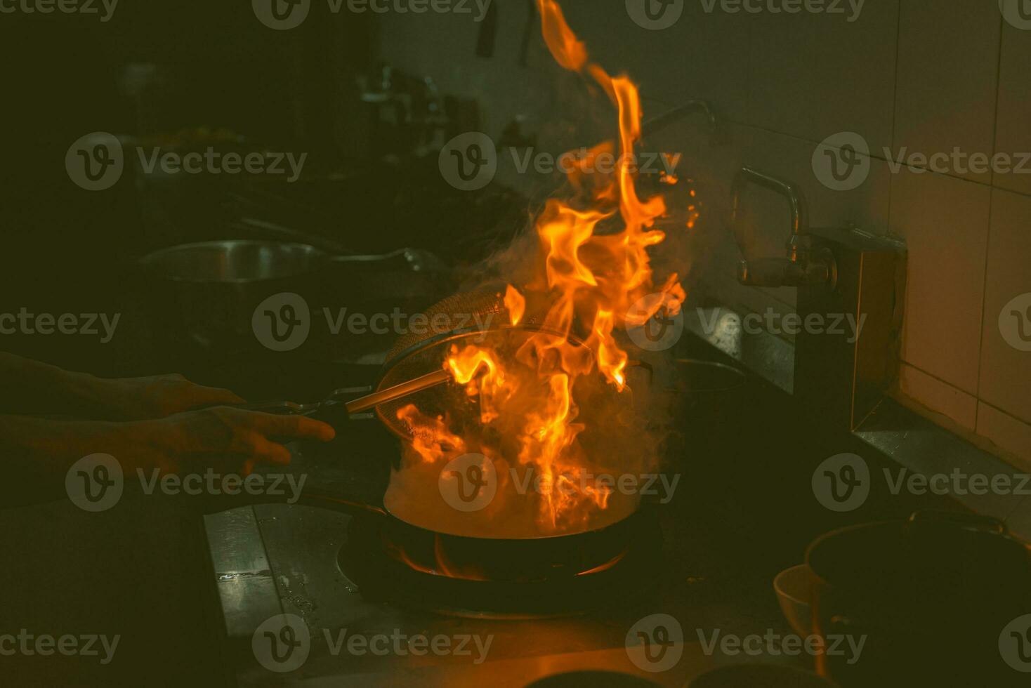 Chef cooking and doing flambe on food in restaurant kitchen photo