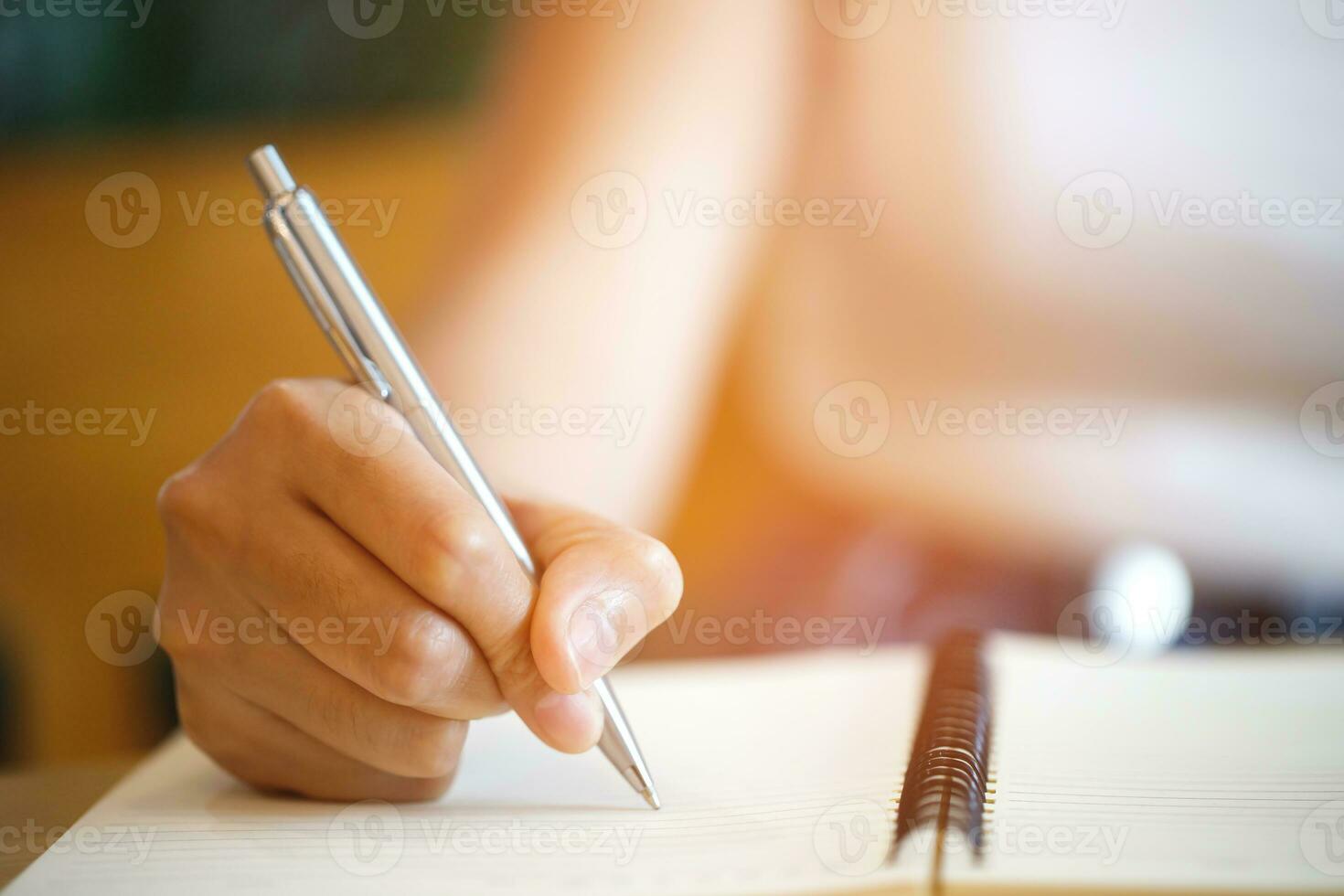close up hand young man are sitting using pen writing Record Lecture note pad into the book on the table wood. photo