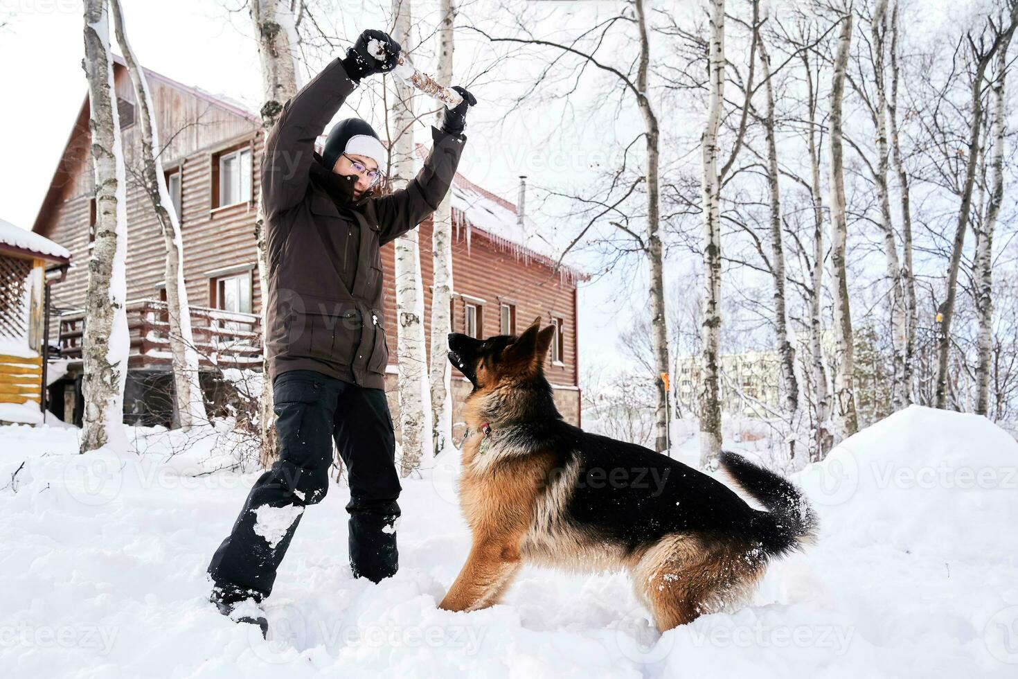 A man plays fetch with a dog in the snowy yard of a house. photo