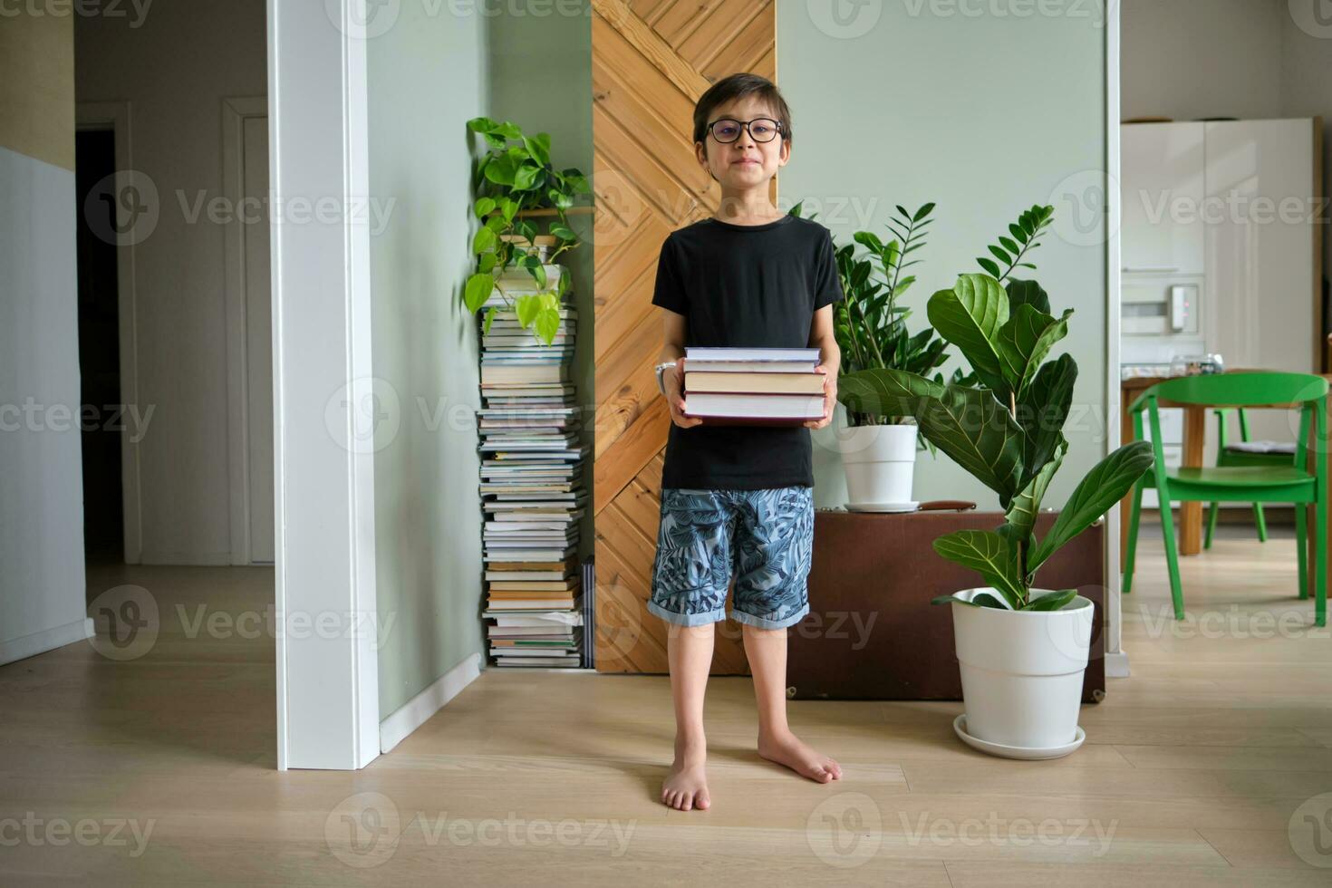 A boy holds a stack of books against the background home library. photo
