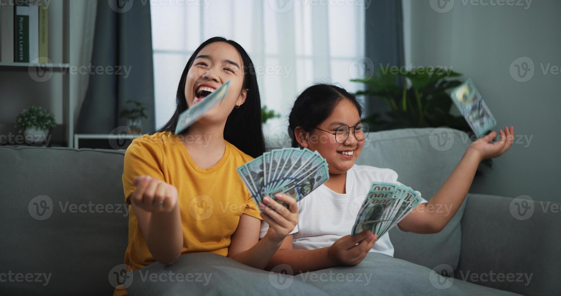Portrait of a young woman and teenage girl enjoying scattering cash bills on a sofa in the living room at home. photo