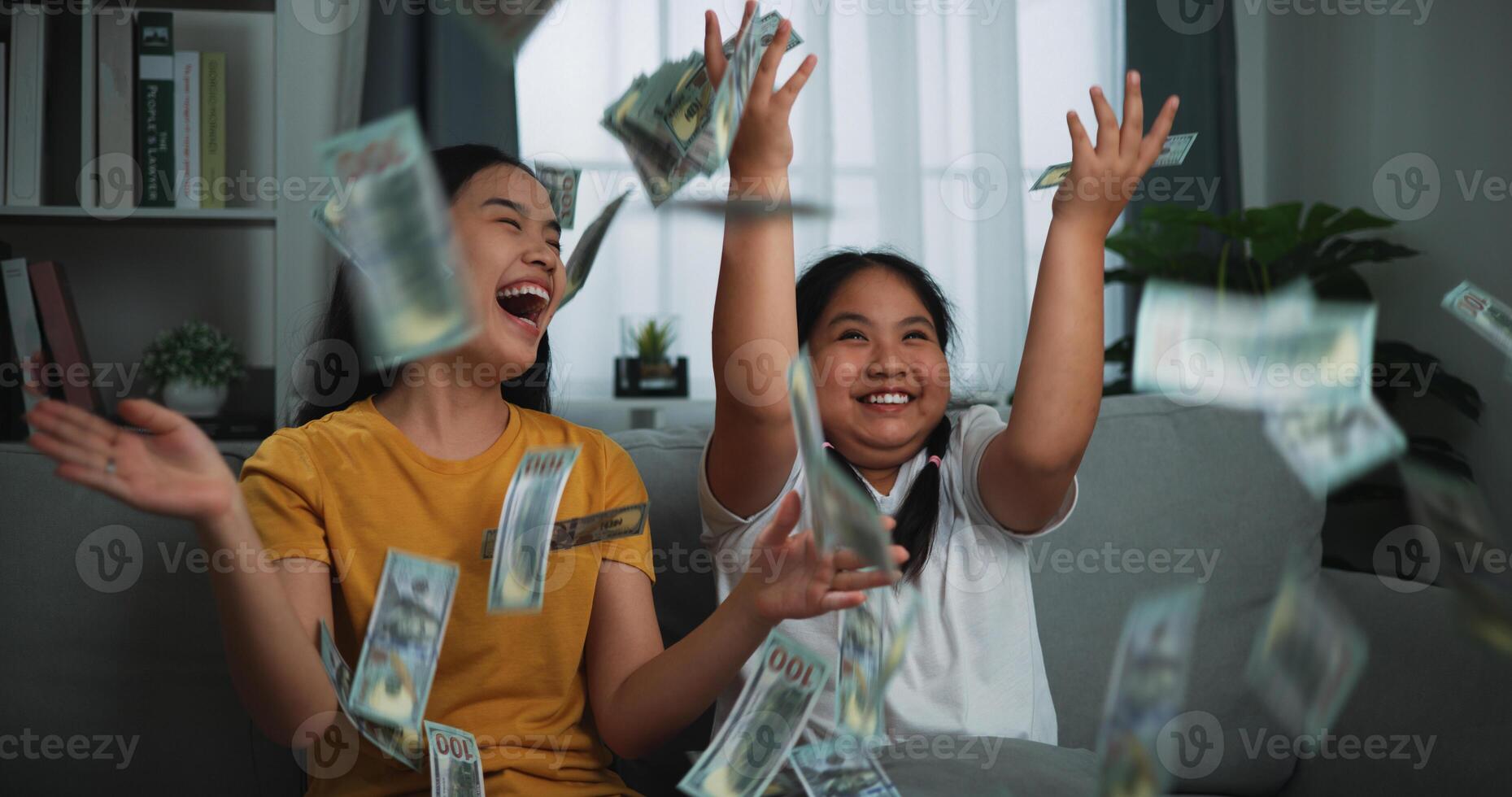 Portrait of a young woman and teenage girl enjoying scattering cash bills on a sofa in the living room at home. photo