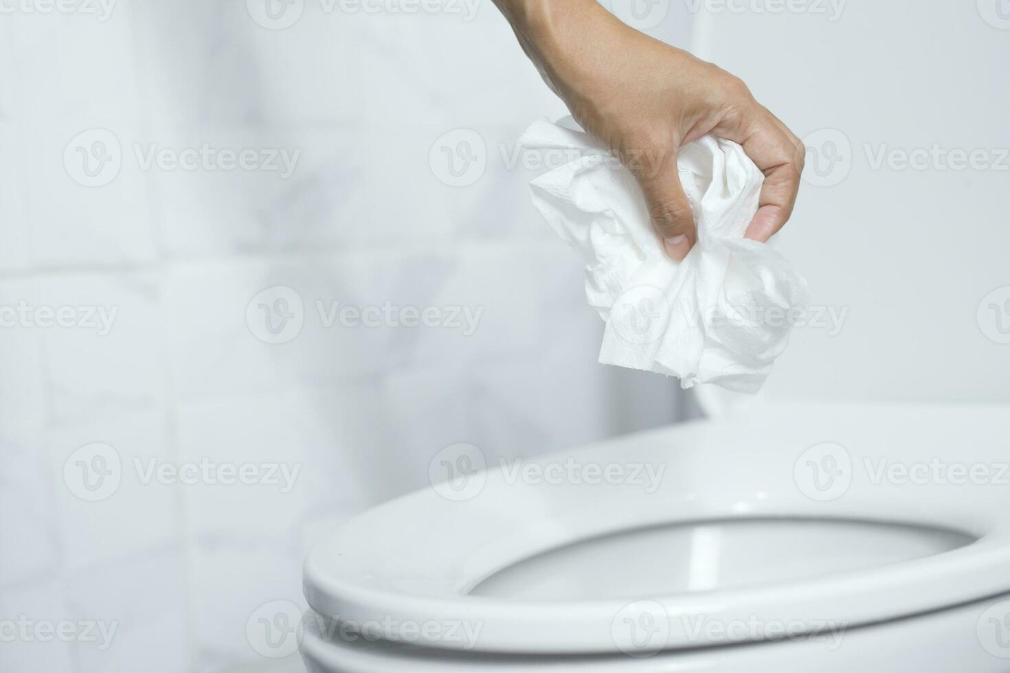 close up hand holding a tissue to be thrown into the toilet bowl. Can