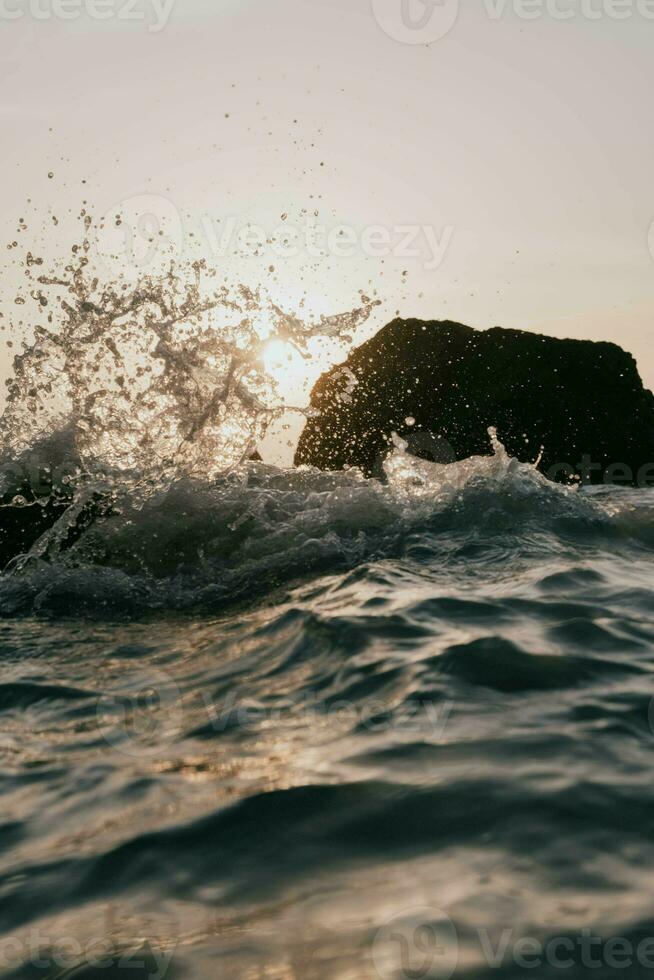 olas estrellarse en el rocas a puesta de sol foto