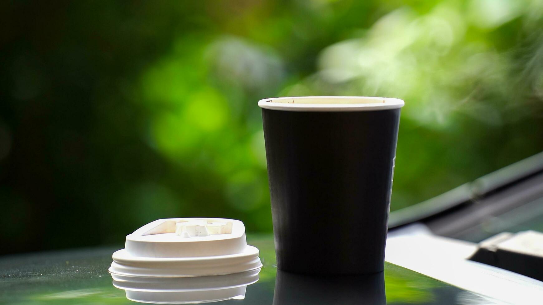 coffee takeaway in a paper cup on top of the car roof green tree background at sunrise in the morning,  selective focus, soft focus. photo