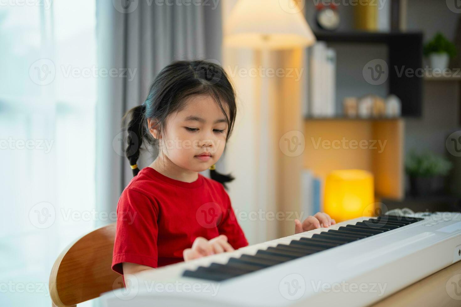 Happy little asian cute baby girl smile playing learning online piano music in living room at home. The idea of activities for child at home during quarantine. Music learning study. photo