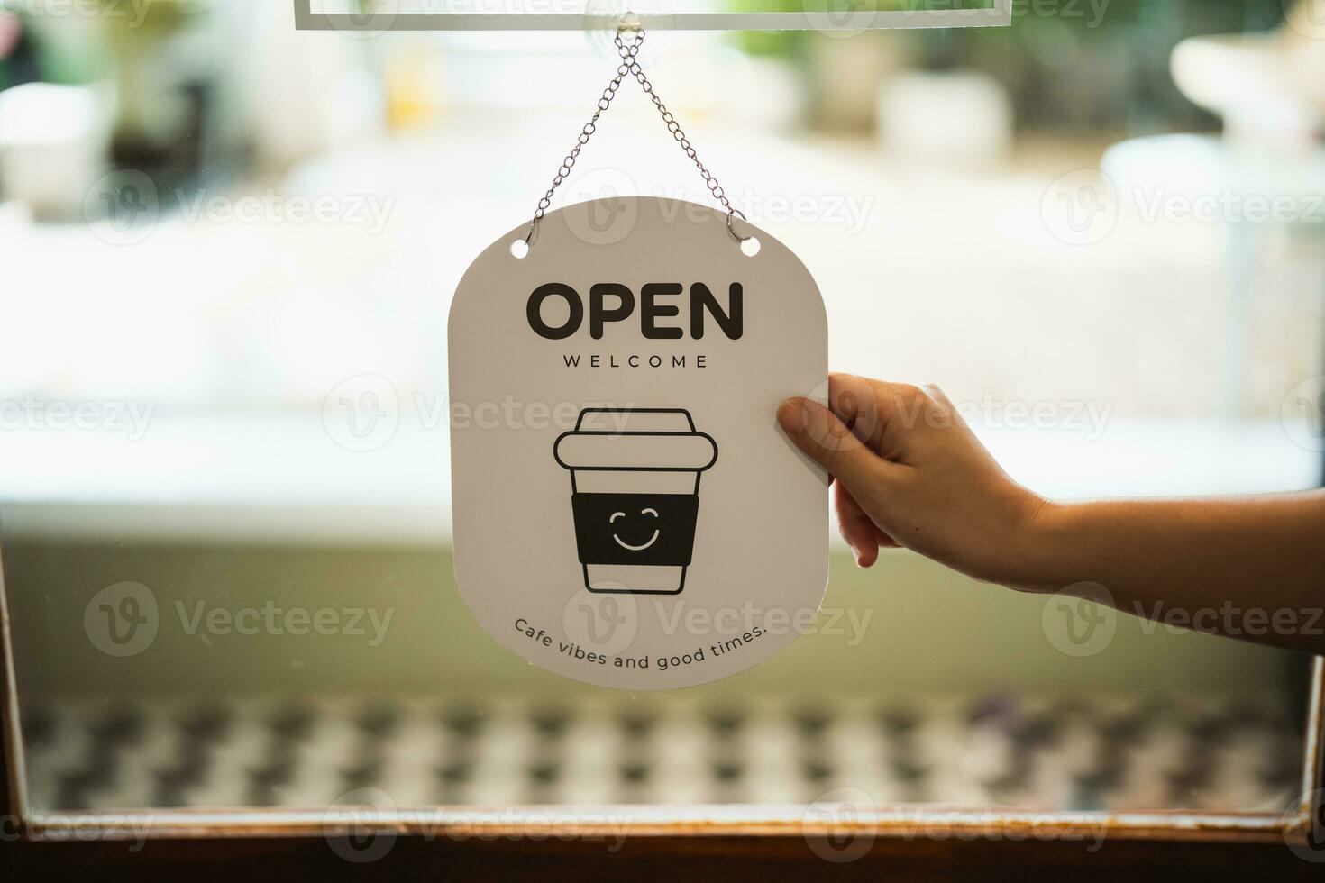 Hand woman hold open sign broad through the door glass. OPEN sign board through the glass of store window. text wooden board door vintage shop sign opened store. photo