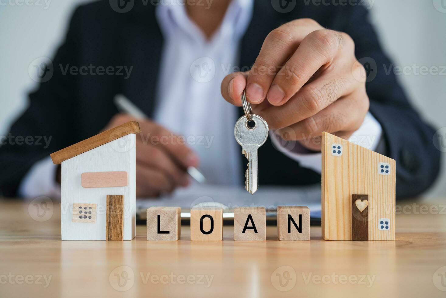 Businessman holding keys, Model house and wood blocks with word LOAN. plan finances investments and savings to buy house real estate.Home on table business accounting and tax and insurance concept. photo