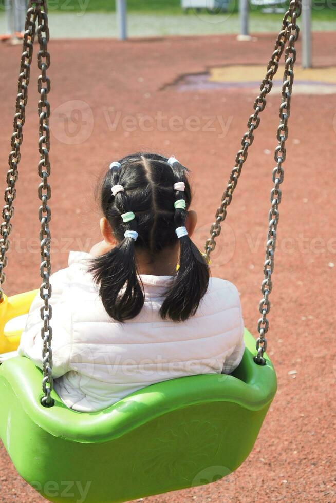 child having fun on a swing on the playground in public park. photo