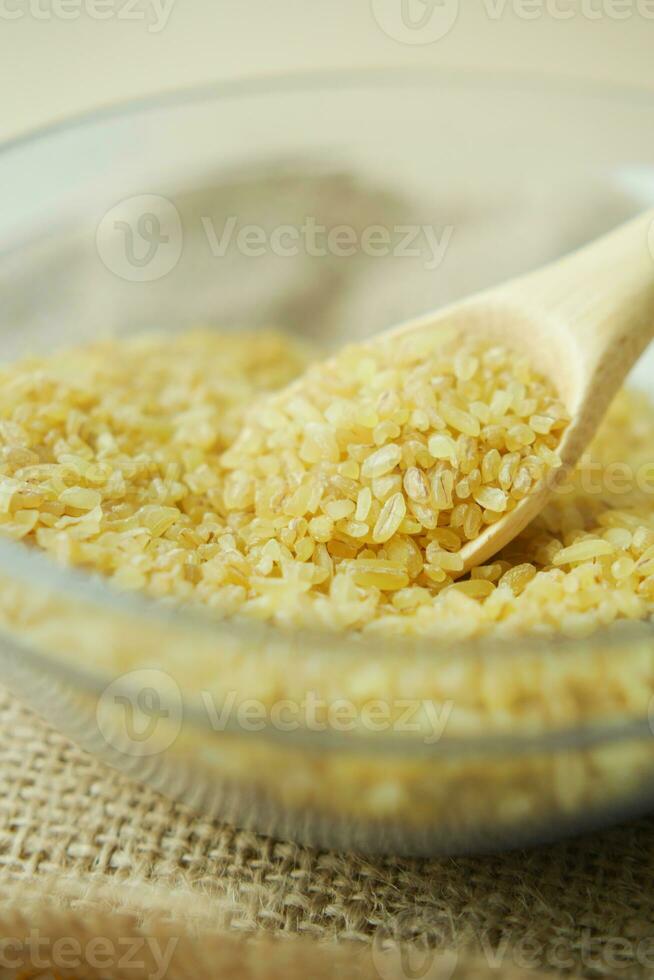 raw bulgur with wooden spoon in a bowl on table photo