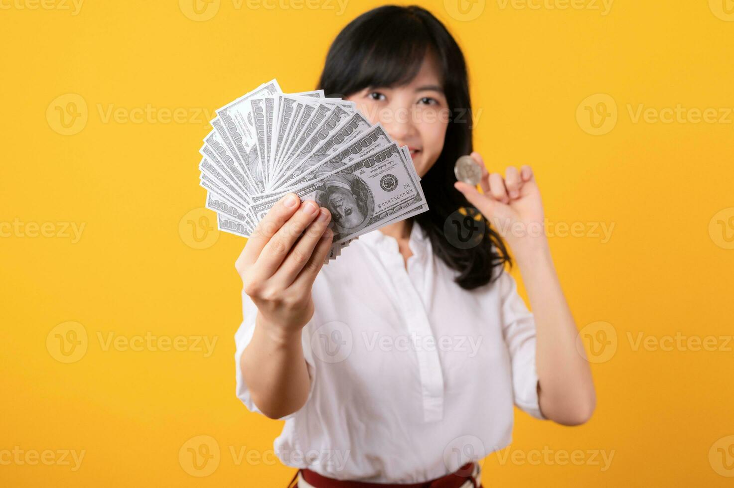 Portrait beautiful young asian woman enterpriser happy smile wearing white shirt and red plants holding cash dollar money and crypto digital currency isolation on yellow background. Wealth concept. photo