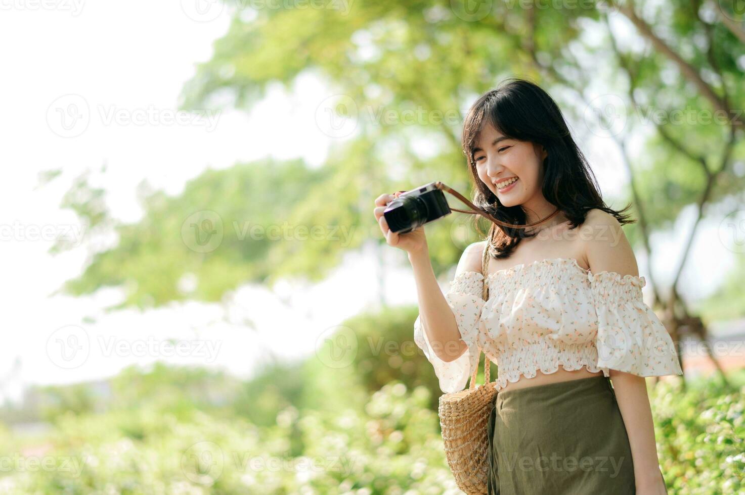 retrato de asiático joven mujer viajero con Costura sombrero y cesta y un cámara en verde público parque naturaleza antecedentes. viaje viaje estilo de vida, mundo viaje explorador o Asia verano turismo concepto. foto