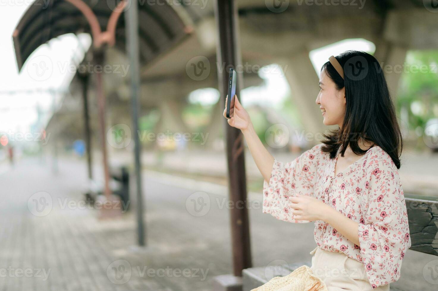 joven asiático mujer viajero con Costura cesta utilizando un móvil teléfono y esperando para tren en tren estación. viaje viaje estilo de vida, mundo viaje explorador o Asia verano turismo concepto. foto