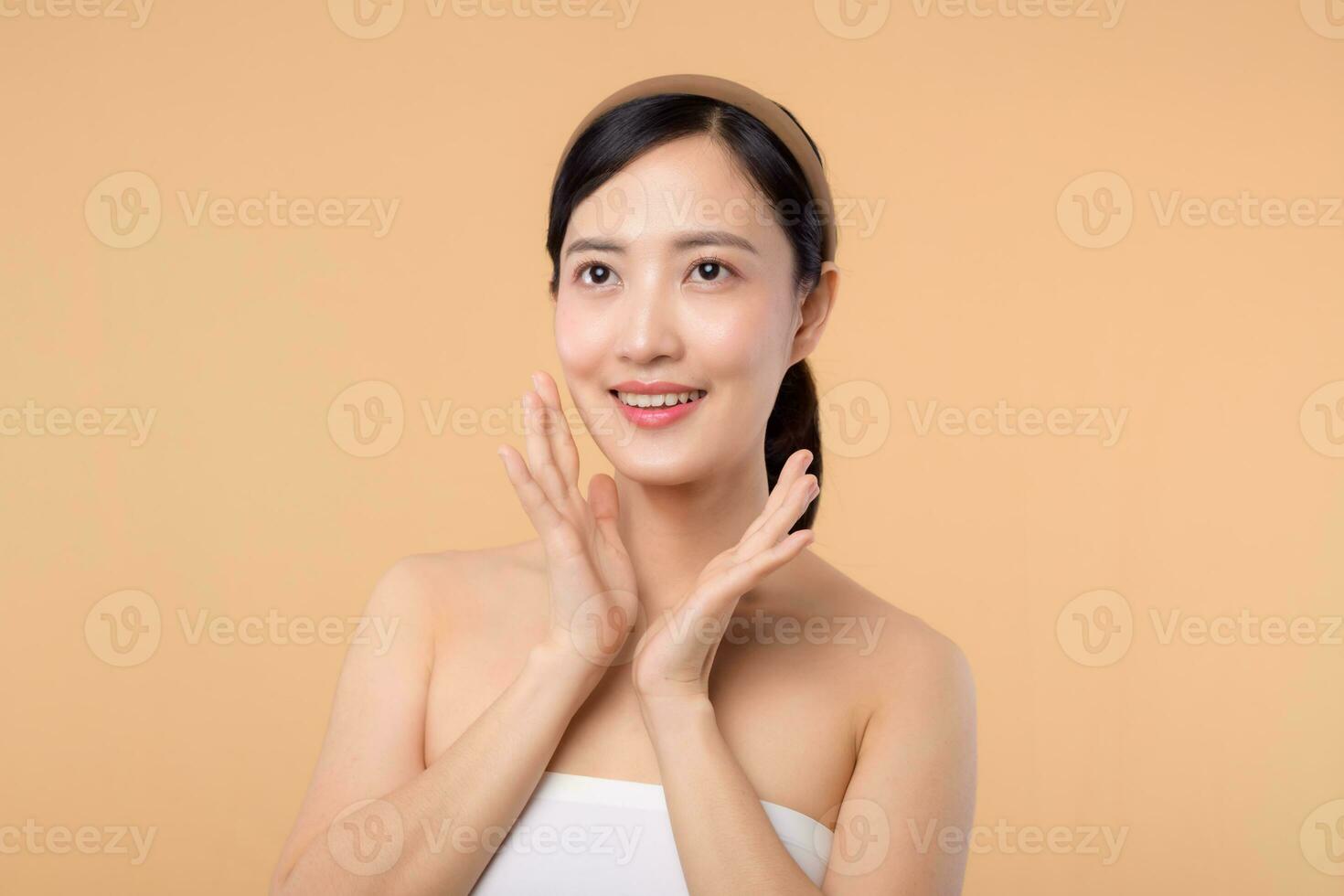 Beautiful girl asian model touching fresh glowing hydrated facial skin on beige background closeup. Beauty face young woman with natural makeup and healthy skin portrait. Skin care concept photo