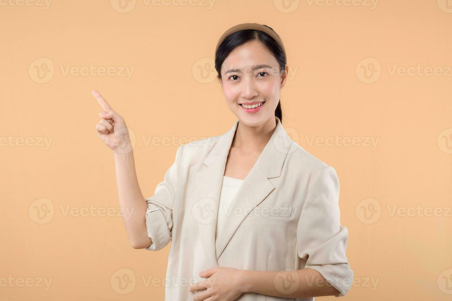 Studio portrait of happy successful confident young asian business woman. Beautiful young lady in white jacket smiling at camera standing isolated on solid beige colour copyspace background photo