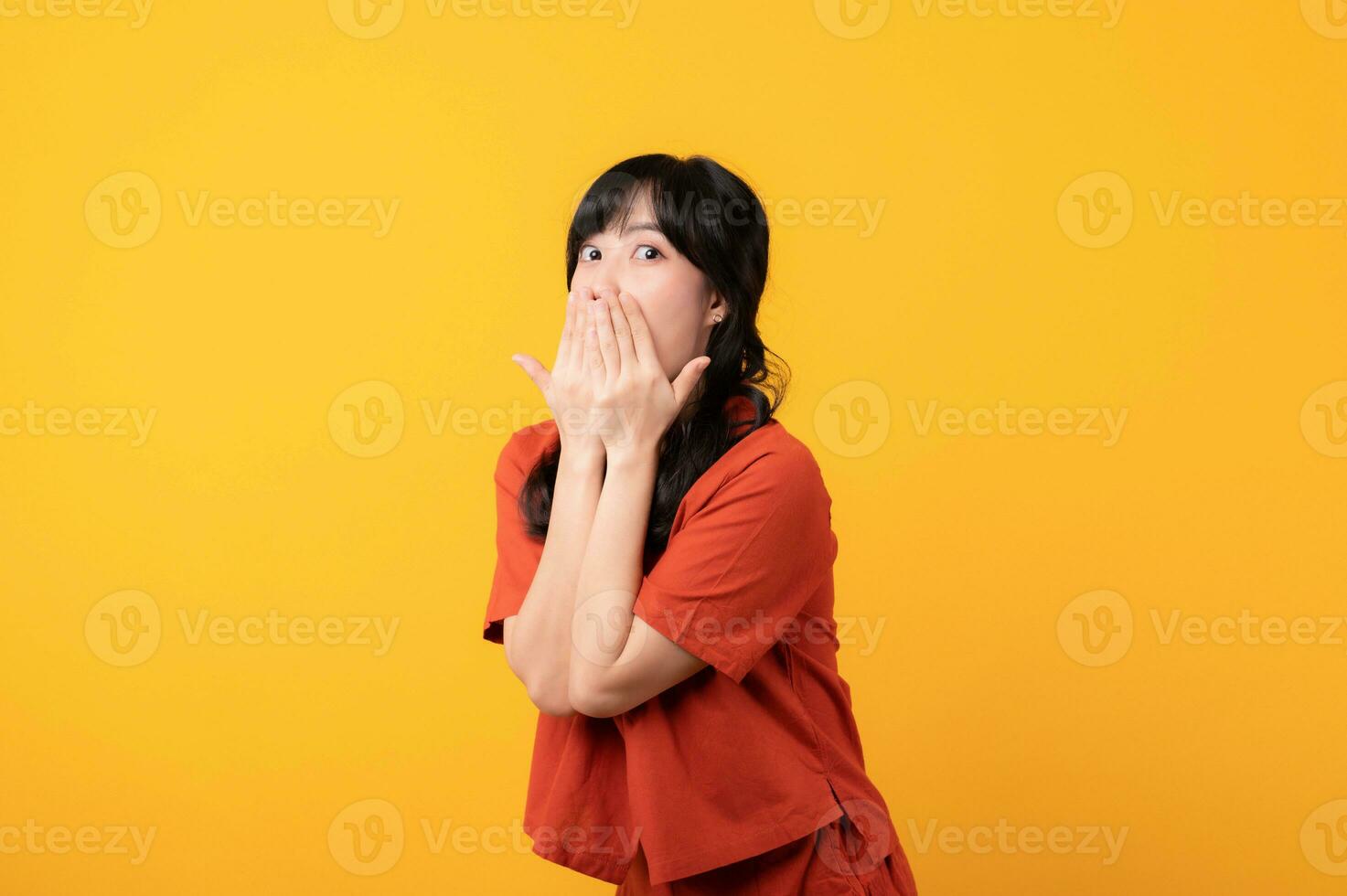 Portrait young beautiful asian woman happy smile dressed in orange clothes looking surprised, reacting amazed, raising eyebrows impressed isolated on yellow studio background. photo