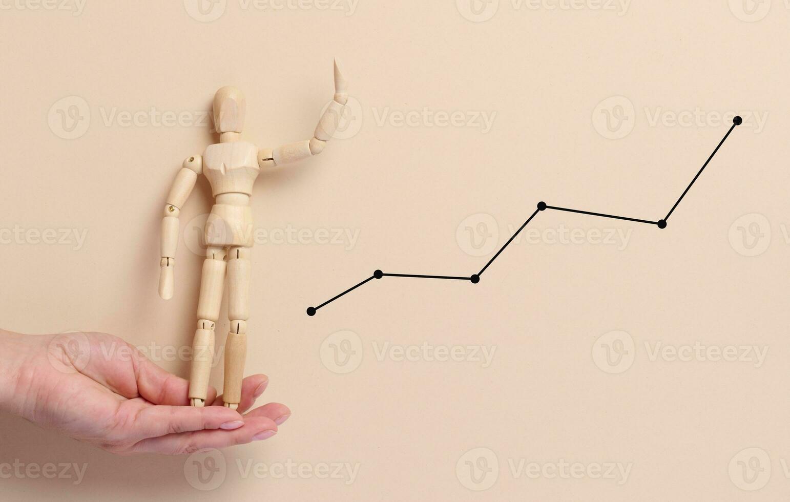 Female hand holding a wooden mannequin on a beige background with a graph photo