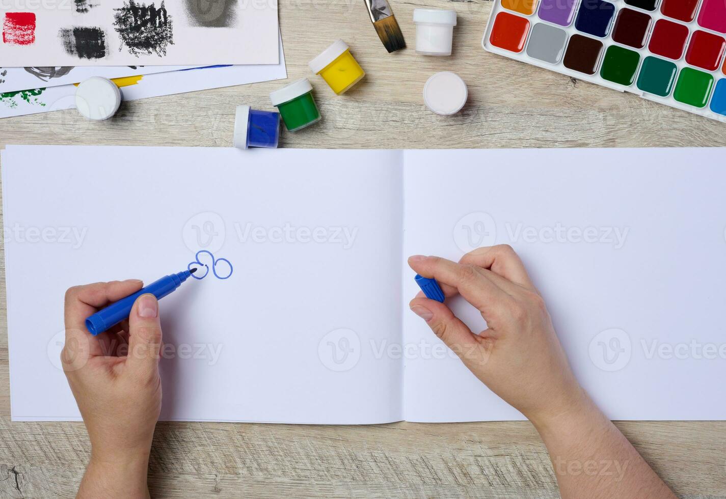 Set of watercolor paints, brushes and paper. Female hands holding a felt-tip pen, top view photo