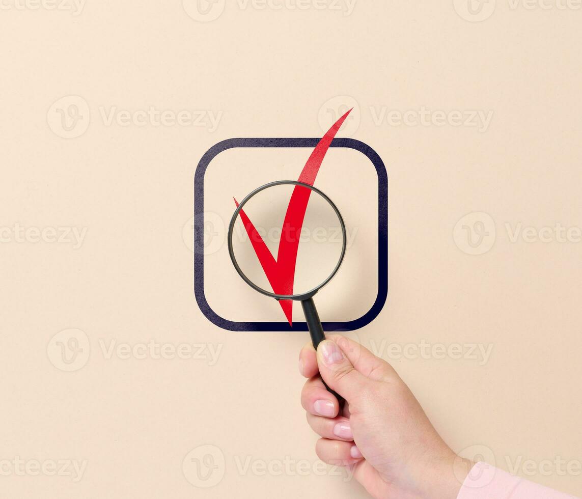 A hand holds a magnifying glass and a sign of approval in a cell. Business approval symbol, yes marks photo