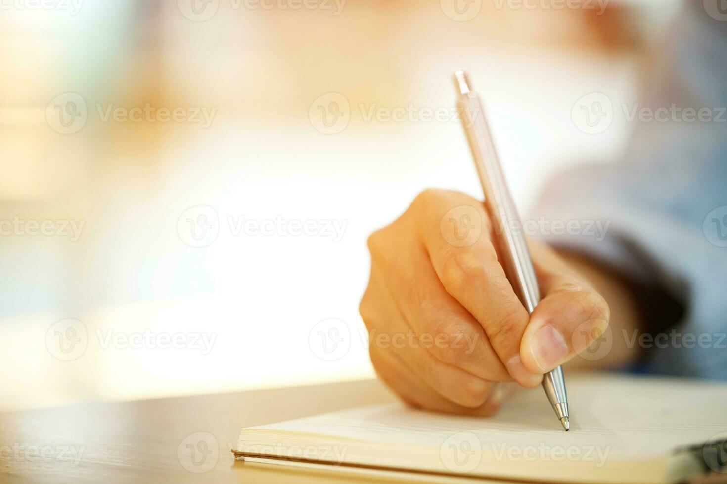 close up hand young man are sitting using pen writing Record Lecture note pad into the book on the table wood. photo