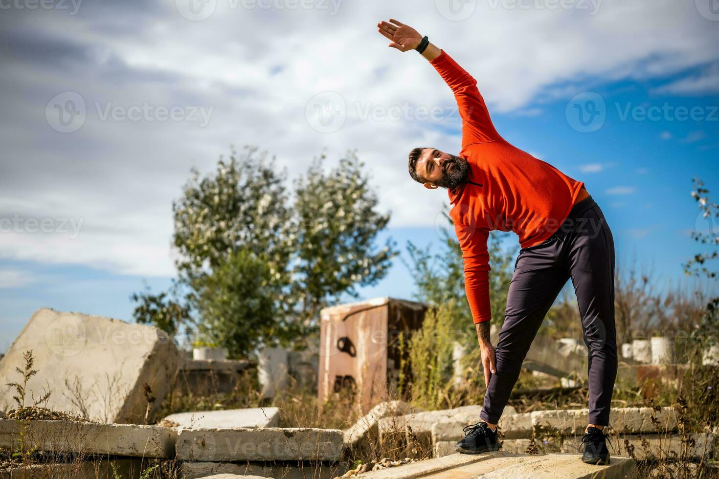 Adult man is exercising outdoor on sunny day. He is stretching his body. photo
