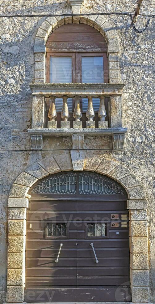 Image of a brown entrance door to a residential building with a stone balcony and window with shutters on a antique facade photo