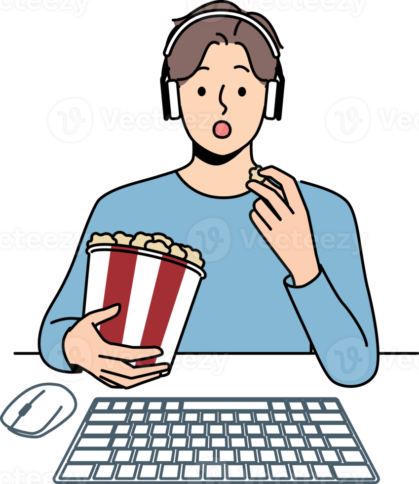 Man with popcorn watches movie sitting at table with computer and looks at screen intrigued png