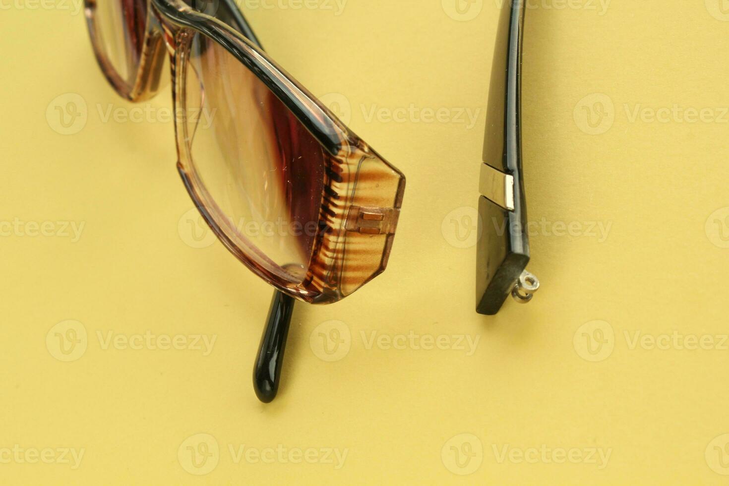 Old broken eyeglasses with damaged legs on orange background. Poor eyesight. Reuse and repair concept. Idea of health. Failure optic eyewear. Breakage of vision correction glasses. Close up, flat lay photo