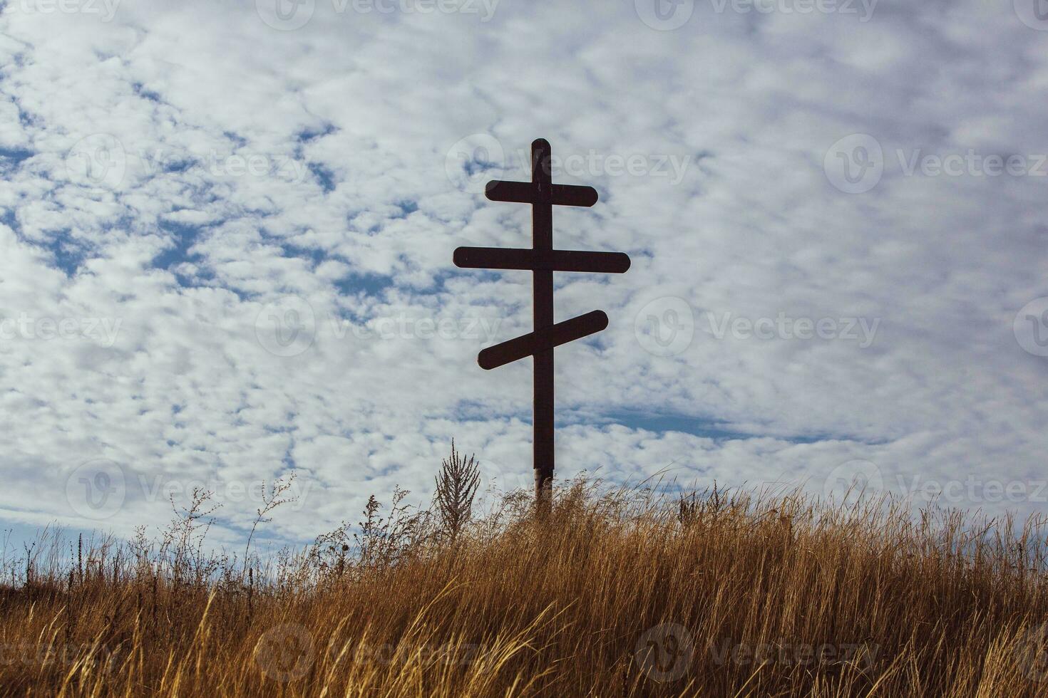 Cross on top of a hill against a blue sky with white clouds. Silhouette of a cross in the field at sunset with dramatic sky. photo